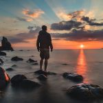 man standing on stone looking at sunset